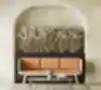 Minimalistinė jauki sėdėjimo zona su modernia kreminės ir oranžinės spalvos sofa prieš tekstūruotą kreminę sieną su niša, papuošta dideliu augalų vazonu su džiovintais pampų žolynais, šalia tamsaus marmuro kavos staliuko ant austinio kreminio kilimo.