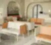 Šiuolaikiška kavinės poilsio zona su minimalistinėmis kreminės ir oranžinės spalvų sofomis, juodo marmuro kavos staliukais, tekstūruotomis kreminėmis sienomis su nišomis ir dideliais augalų vazonais su džiovintais pampų žolynais, sukurianti šiltą ir jaukią kavinės, registratūros ar laukimo zoną.