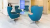 Moderni Nordclinic klinikos laukiamoji erdvė su ryškiai mėlynomis kėdėmis, stiklo staliuku ir šiuolaikiniu interjeru.