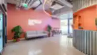 SHED Co-living Vilnius registratūros erdvė su koraline siena, metaliniu stalu, industrinėmis lubomis ir poilsio sofa.