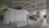 Minkštasuolių kompozicija prie betoninės pertvaros moderniame biure su apvaliais šviestuvais.