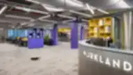 Plati moderni WORKLAND | VILNIUS, BURĖS biuro erdvė su ryškiai violetiniais stulpais, geltonomis lentynomis, pilku kilimu ir aptarnavimo balkonu prie įėjimo.