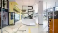 Modernus KTU bibliotekos interjeras su informaciniu stalu, stiklinėmis sienomis ir krypties žymėjimais grindyse.