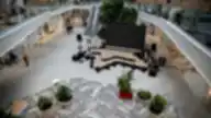 Vilnius Outlet viešoji erdvė su centrine scena, dideliu LED ekranu ir aplink išdėstytais augalais bei moderniu prekybos centro interjeru.