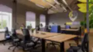 Co-working “Magnēts” šviesi erdvė su mediniais darbo stalais, ergonominėmis kėdėmis, žaliomis augalų detalėmis ir logotipu ant sienos.