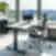 Citadele privatus biuras su reguliuojamo aukščio tamsaus medžio stalu, ergonomiška juoda tinklelio sukamoji kėde, žema juoda spintele po panoraminiais langais su vaizdu į upę ir miesto panoramą bei aukšta vazonine gyvyne.