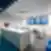 Moderni „New Crush“ biuro poilsio zona su balta virtuvės sala, LED žiediniu šviestuvu, mėlynomis grindimis ir stalo zona su kėdėmis