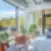 Šviesi SHED Co-living Vilnius poilsio erdvė su vazoniniais augalais ir pastelinėmis kėdėmis, dideliais langais ir išėjimu į terasą su vaizdu į mišką.
