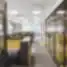 Modernus DHL Lietuva atviro plano biuras su eilėmis darbo stalų, geltonomis akustinėmis pertvaromis ir stiklinėmis kabinomis, kylančiomis iš pilkos ir geltonos kiliminės dangos, tarpai atskirti juodos metalinės grotelės panelėmis.