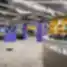 Plati moderni WORKLAND | VILNIUS, BURĖS biuro erdvė su ryškiai violetiniais stulpais, geltonomis lentynomis, pilku kilimu ir aptarnavimo balkonu prie įėjimo.