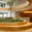 Modernus biuro vestibiulis su centrine apvalia žalumos sala ir recepcijos stalu fone.