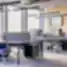 HRMNY šiuolaikinis biuras su ergonomiškomis darbo vietomis, šviesiomis medžiagomis ir akcentine mėlyna šviesa lentynose