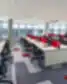 Atvira Citadele biuro erdvė su eilėmis šviesaus medžio stalų, raudonais audinių privatumo skirtukais, ergonomiškomis juodomis sukamosiomis kėdėmis, panoraminiais langais su žaliuzėmis ir geometrišku kilimėlio raštu po linijiniu pakabinamu apšvietimu.