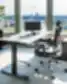 Citadele privatus biuras su reguliuojamo aukščio tamsaus medžio stalu, ergonomiška juoda tinklelio sukamoji kėde, žema juoda spintele po panoraminiais langais su vaizdu į upę ir miesto panoramą bei aukšta vazonine gyvyne.