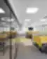 Modernus DHL Lietuva atviro plano biuras su eilėmis darbo stalų, geltonomis akustinėmis pertvaromis ir stiklinėmis kabinomis, kylančiomis iš pilkos ir geltonos kiliminės dangos, tarpai atskirti juodos metalinės grotelės panelėmis.