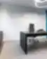 Juodas New Crush vadovo stalas su ergonomine kėde, baltomis sienomis, mėlynu akustiniu lubų bėgiu, rožiniu pliušiniu flamingu ant spintelės ir neono užrašu „We make things happen“