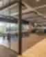 Revolut moderni biuro poilsio ir bendradarbiavimo zona su stikline susitikimų kabina, aukštu bendru stalu su taburetėmis prie panoraminių langų, atvira poilsio erdvė su moduline sėdimąja dale, šviesaus medžio žvynelinė flooring ir atvira akustinė lubų konstrukcija.