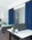 Wallter biuro dizainas, bendras darbo kambarys, balti stalai, pilkos pertvaros, žalios biuro kėdės, geltona grindų lempa, mėlynos užuolaidos, kubinės lentynos.
