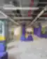 Atvira ir spalvinga WORKLAND | VILNIUS, BURĖS bendradarbiavimo erdvė su violetiniais stulpais, pilkais kilimais, geltonomis lentynomis ir moderniais, moduliniais violetinės spalvos minkštais sėdimaisiais baldais.