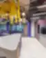 Šiuolaikiška WORKLAND | VILNIUS, BURĖS bendrojo naudojimo virtuvėlė su ilga balta sala, violetiniais stalviršiais, geltonais lubų pakabinimais, neoniniu „Better together!“ užrašu ir moderniomis poilsio zonos violetinėmis sofos dalimis.