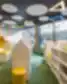 Balsių mokyklos bibliotekoje – spalvinga ir šviesi erdvė su moderniais baldais ir geometriniais šviestuvais.