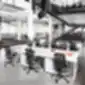 Kelios juodos ergonomiškos biuro kėdės prie stalų atviroje erdvėje.